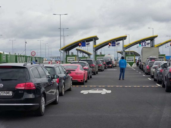 Autók sorakoznak a autópálya-határátkelőnél több sávban, ellenőrzésre várva, felhős időben.
